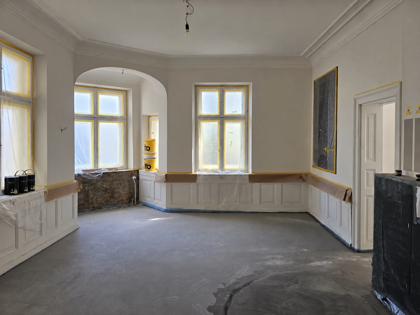 Altbauraum während der Innenausbauarbeiten mit Stuck, Wandvertäfelung und abgeklebten Fenstern; Foto KI-ausgerichtet